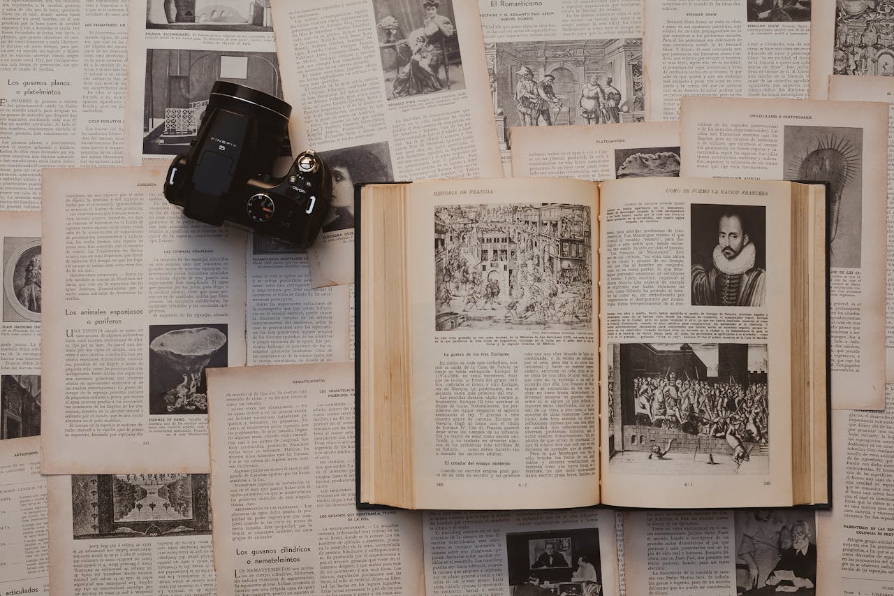 A flat lay of an open book and vintage camera surrounded by historical pages, emphasizing culture and education.