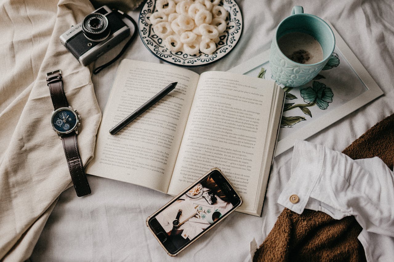 A cozy flatlay featuring a book, coffee, and personal items like a camera and watch.